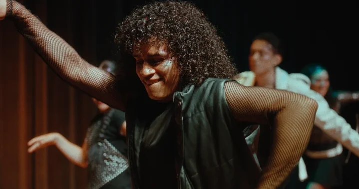 Bailarín de rizos en plena coreografía, con el grupo detrás