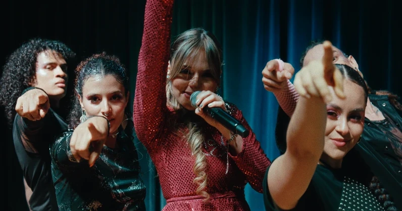 Naty Borda cantando con la mano en alto mientras cuatro bailarines señalan a la cámara