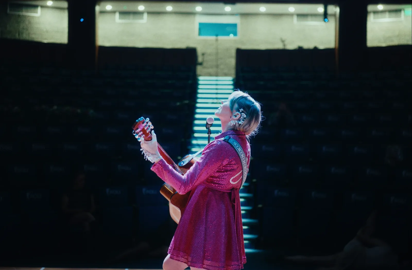 Naty Borda con la guitarra mirando hacia arriba en el escenario, con el auditorio de fondo