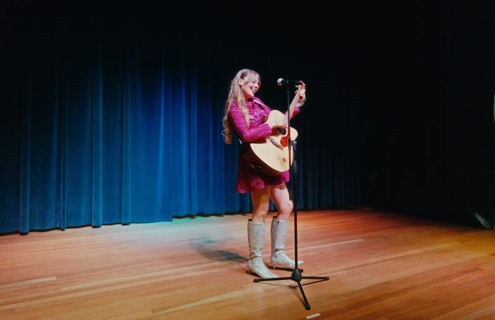 Naty Borda tocando la guitarra sola en el escenario, con botas plateadas